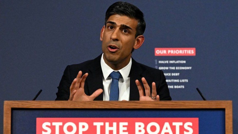 Rishi Sunak stands at a podium with the slogan 'stop the boats'