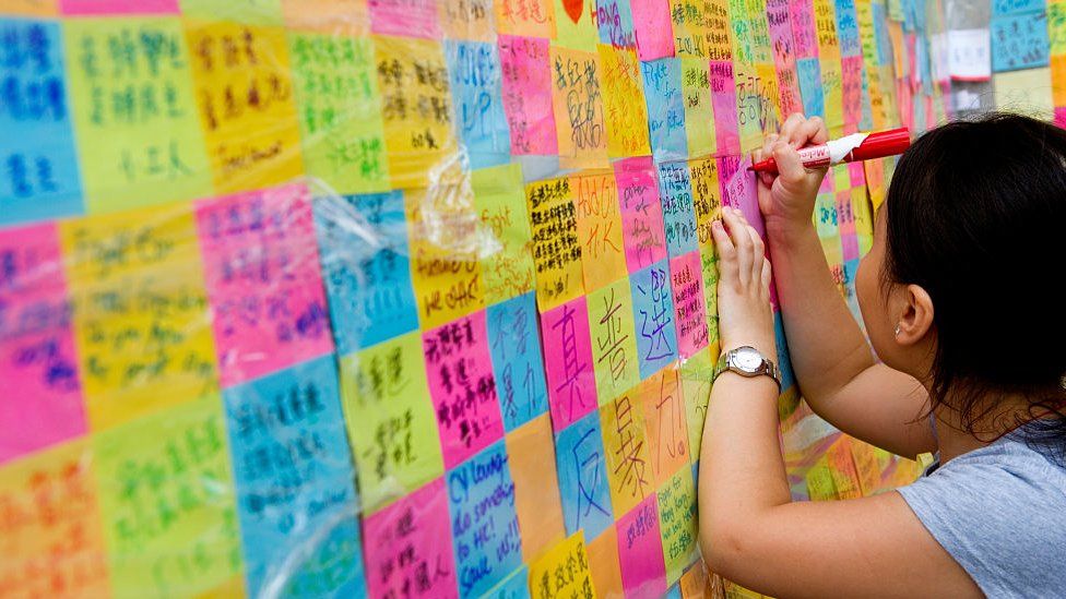 A little girl writes on a stick-up note to be hung on a wall, Hong Kong 2014