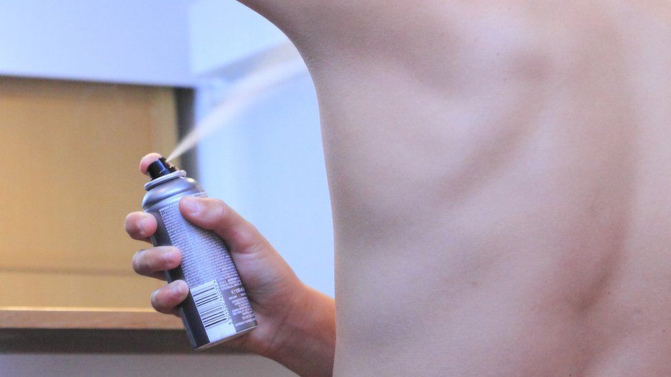Teenage boy spraying himself with deodorant