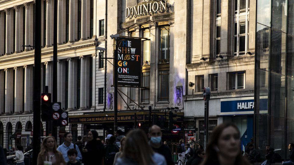 Crowds in front of the Dominion Theatre with a sign saying The Show Must Go On