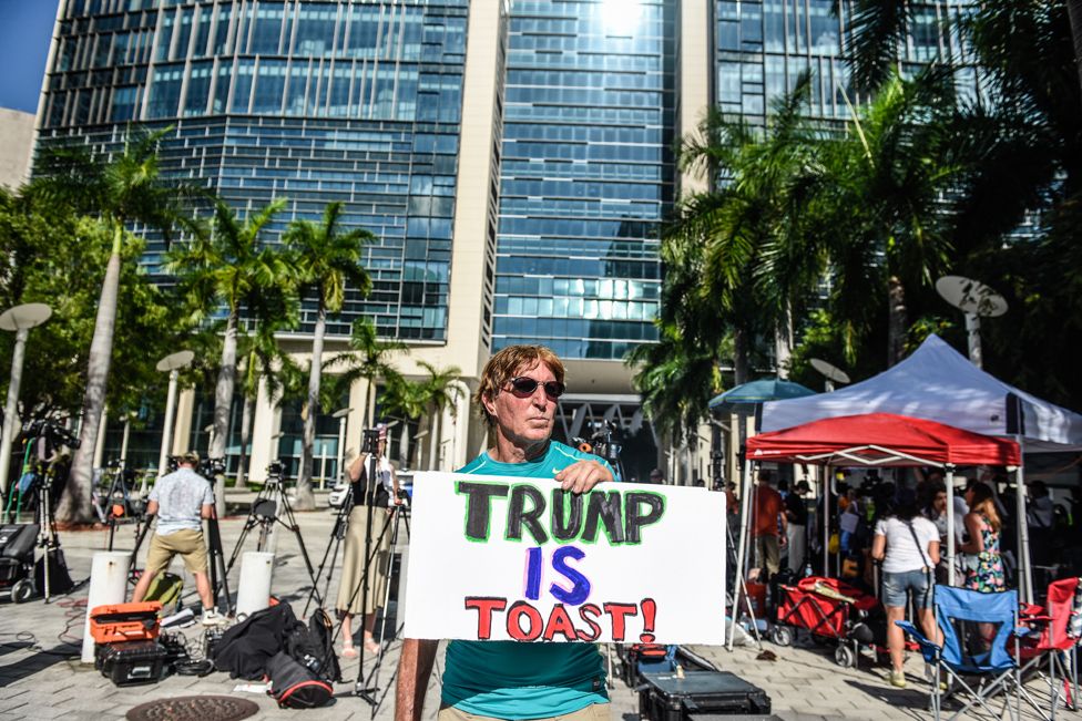 Протестующий против бывшего президента США Дональда Трампа держит табличку у здания Федерального суда США Уилки Д. Фергюсона-младшего, где Трампу должны предстать перед судом в тот же день 13 июня 2023 года в Майами, Флорида