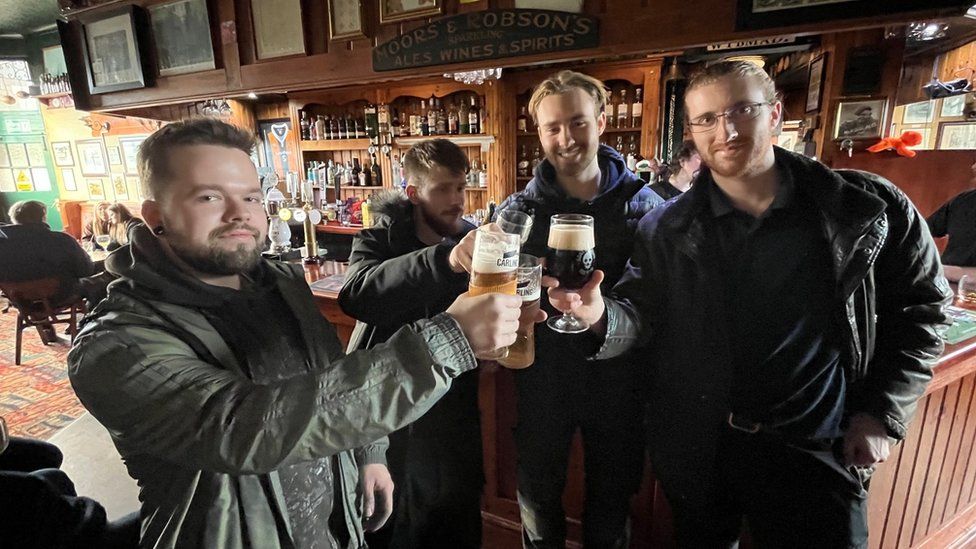 Four young men raise their glasses at the bar