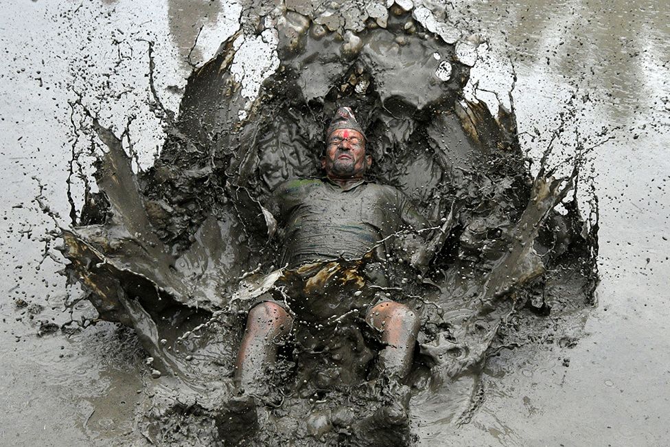 A mud-covered farmer plays in a rice paddy field during National Paddy Day, which marks the start of the annual rice-planting season, in Tokha village on the outskirts of Kathmandu, Nepal, on 19 June 2022