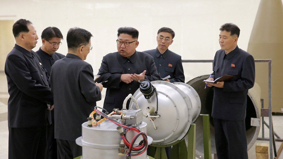 Kim Jong-un, centre, gestures at men in dark military suits over what appears to be a complicated bomb or warhead