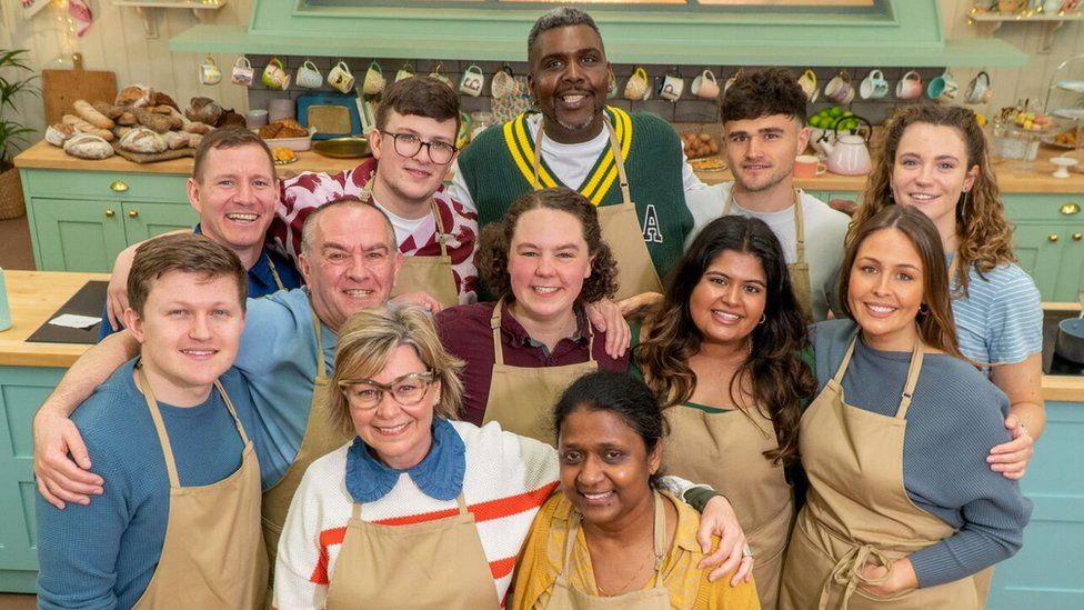 Twelve Great British Bake Off contestants pose for a photo together in three rows