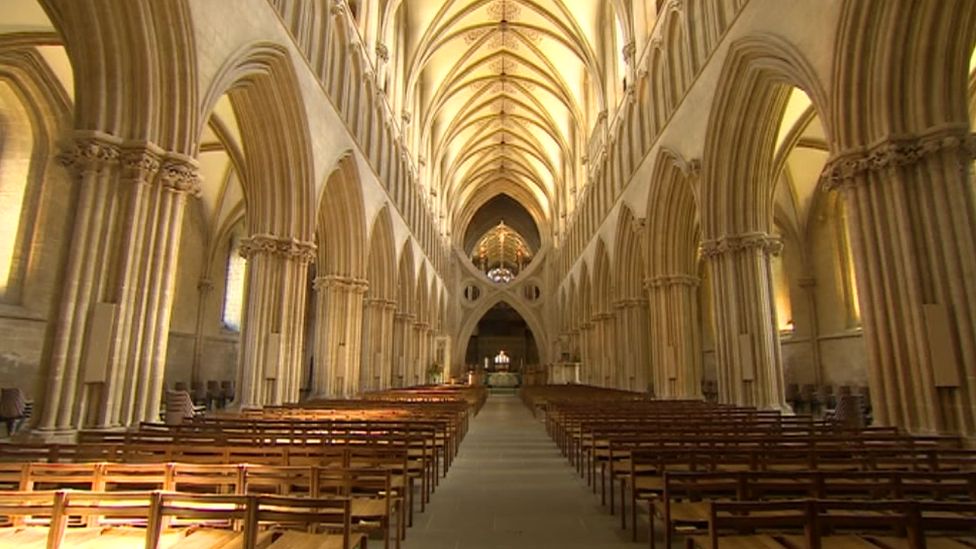 An inside shot of Wells Cathedral, with lots of empty chairs and the alter further down the alisle