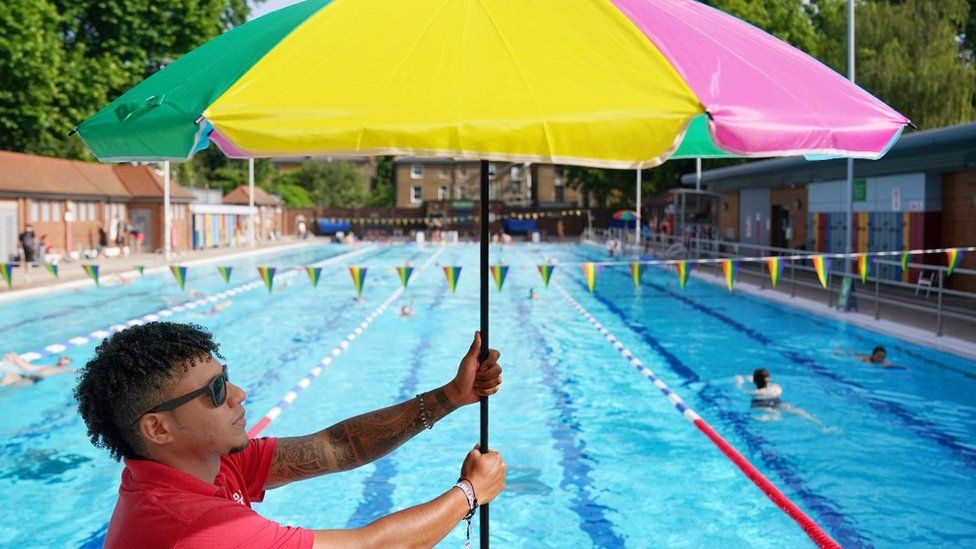Staff member David Jimenez erects an umbrella as people take to the water for an early morning cool down at London Fields Lido, in Hackney,