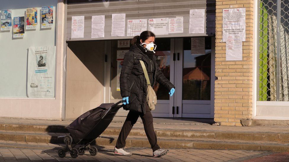A woman protected with a mask and gloves walks past a public employment office
