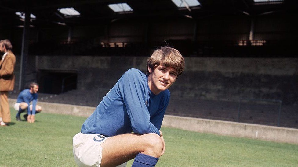 Trevor Whymark in a blue Ipswich Town shirt and white shorts. He is kneeling on a football pith