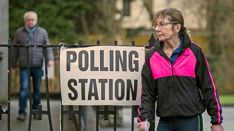 A woman stands by a sign for a polling station in Northern Ireland