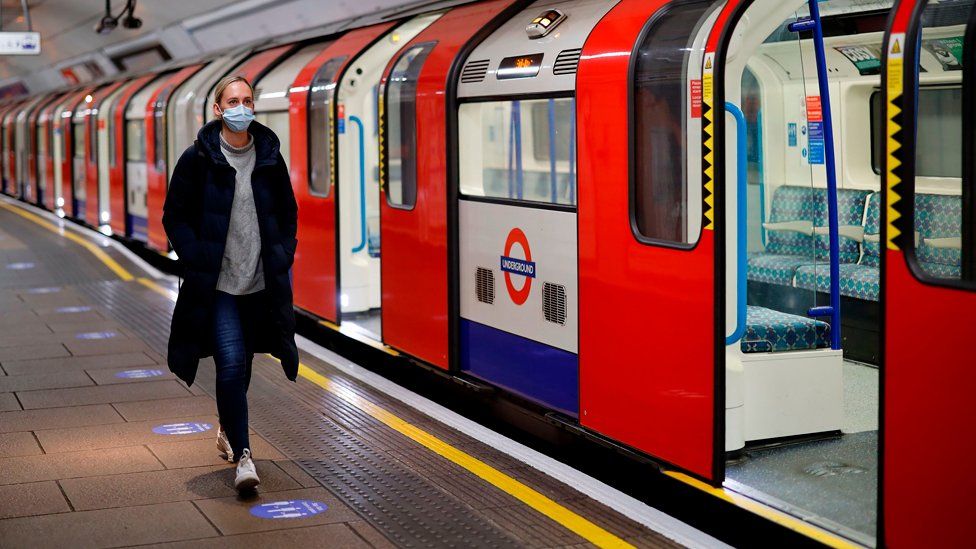 A woman wearing PPE (personal protective equipment), including a face mask as a precautionary measure against COVID-19, walks along the platform alongside a London Underground Tube train in the morning rush hour, on May 11, 2020