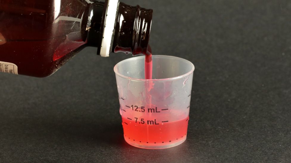 Liquid cough syrup being poured into a small measuring cup