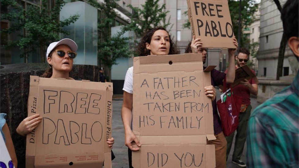 Protesters with pizza box signs reading "free Pablo", "A father has been taken from his family"