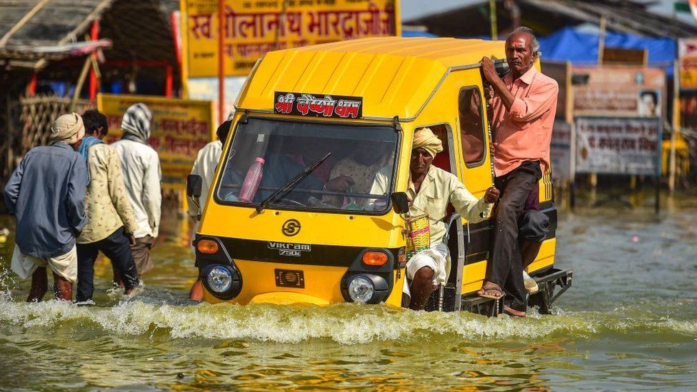 People wade through a flooded path near Sangam, the confluence of the Ganges, Yamuna and mythical Saraswati rivers after the water level of river Ganges and river Yamuna rose, in Allahabad on October 14, 2022.