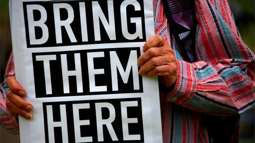 A protester holds a sign saying "bring them here"
