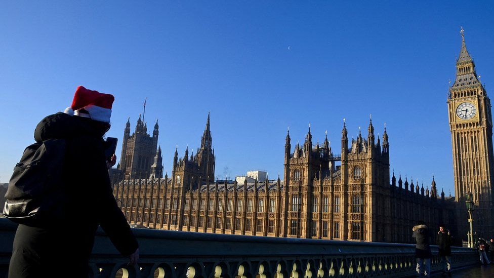 A woman wearing a Santa hat walks towards the Palace of Westminster