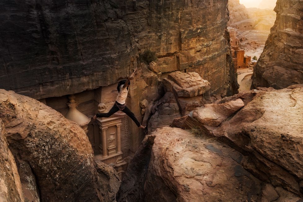 A Bedouin jumps over a small gorge between rocks in ancient Petra, Jordan.
