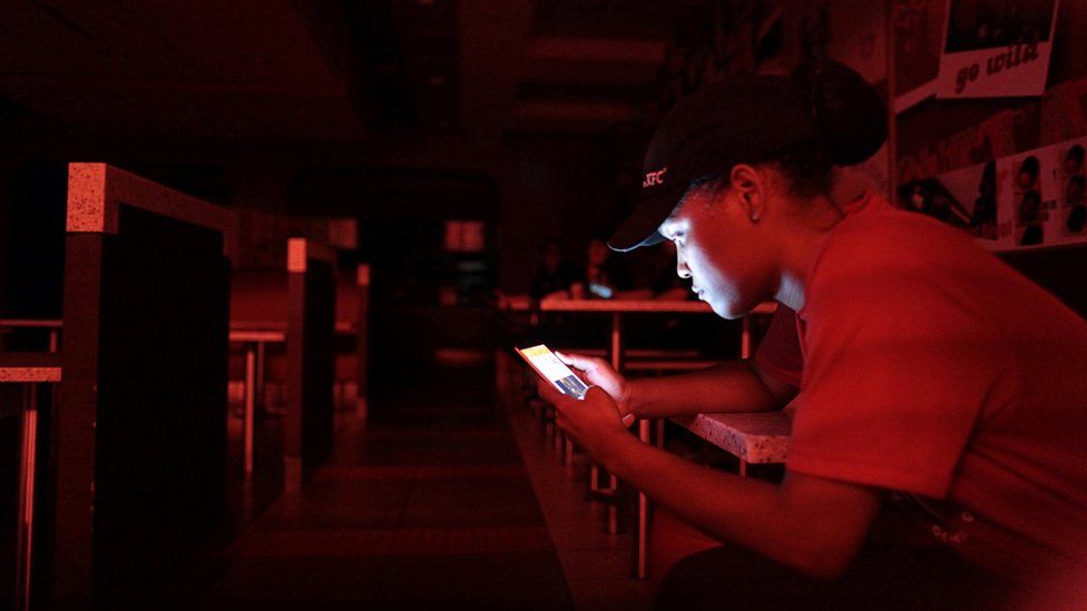An employee at a fast-food restaurant in a shopping mall uses her mobile phone during a power outage in San Juan, Puerto Rico, on 21 September