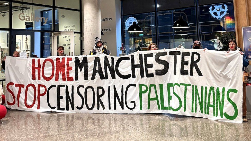 Artists hold banner saying "Home Manchester stop censoring Palestinians"