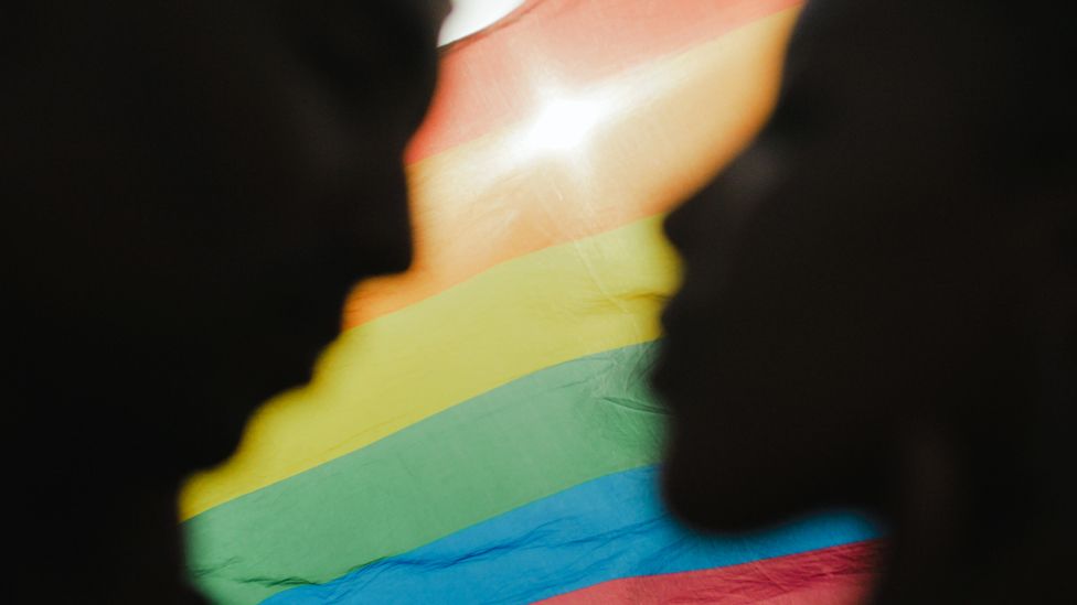A silhouette of two people in front of a rainbow flag