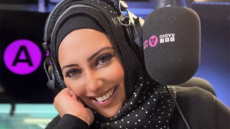 Nadia Ali smiling in the studio, she is next to an Asian Network microphone, and wearing a hijab, with is patterned with polka dots.