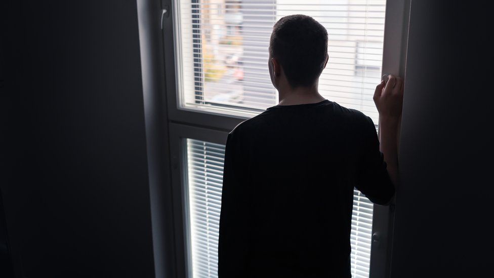 Anonymous man gazes out of a window with his back facing the camera.