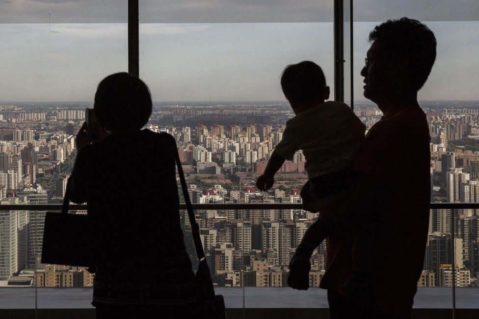 A Chinese couple stand with their child as they look out on residential and office buildings from a luxury hotel on June 11, 2015 in Beijing, China.