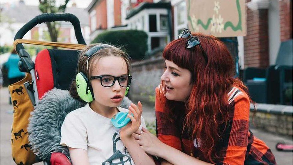 Mother Laura with her son Oscar. Oscar is in a wheelchair wearing ear defenders whilst his mum looks at him dotingly.