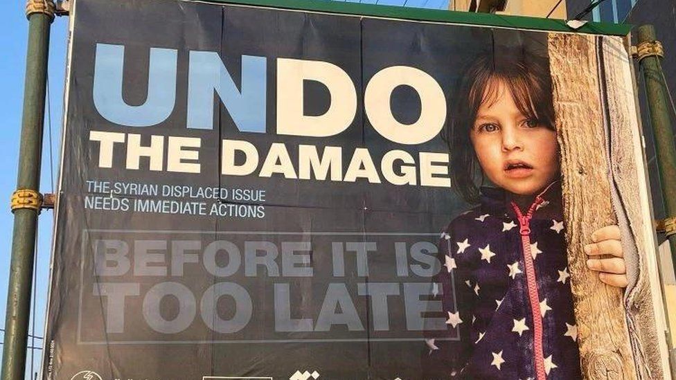 A billboard featuring a little girl next to large blue and white lettering saying 'undo the damage'.