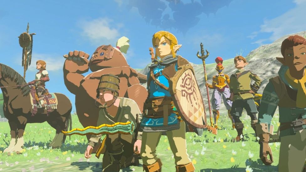 Screenshot of Tears of the Kingdom with silent protagonist Link pictured alongside villagers and monsters from the game. Link is an elfish character with blonde hair and blue eye. He wears traditional blue and green robes and carries a shield and weapons.