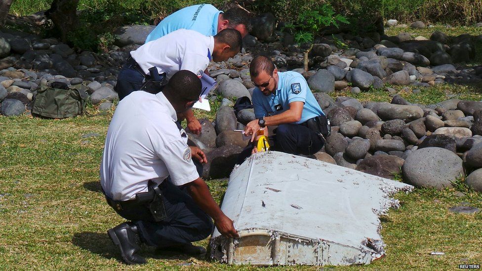 French gendarmes and police inspect a large piece of plane debris which was found on the beach in Saint-Andre, on the French Indian Ocean island of La Reunion (29 July 2015)