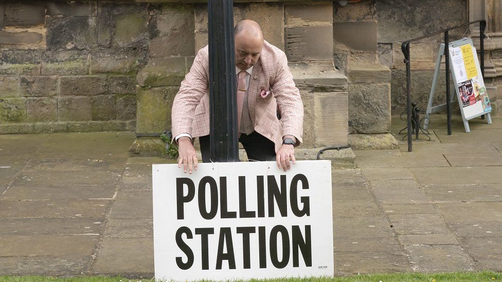 A polling station sign is adjusted outside the polling station