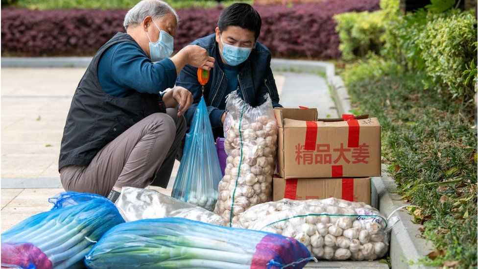 Two residents give shares of the garlics and green onions in a compound during a Covid-19 lockdown, in Pudong district in Shanghai on April 15, 2022.
