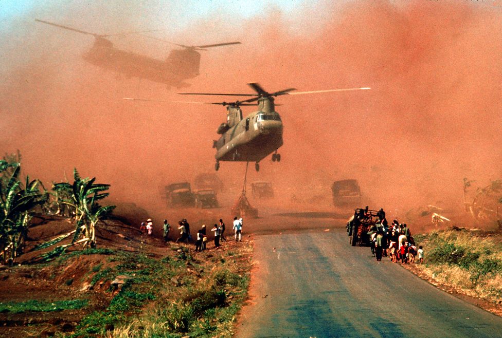 Two Chinook helicopters hover above a road as they assist in evacuating supplies and soldiers of the South Vietnamese (ARVN) 18th Division and their families from Xuan Loc, Vietnam, mid April, 1975.