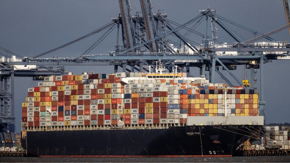 A container ship berthing, stacked high with cargo