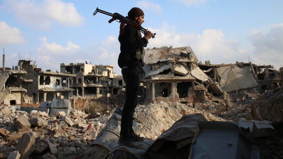 Боец повстанцев стоит среди обломков разрушенных зданий в контролируемом повстанцами районе Дераа на юге Сирии, 14 марта 2017 г.
