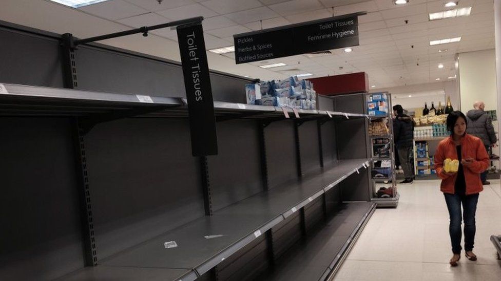 A shopper passes empty shelves at a Waitrose supermarket in London