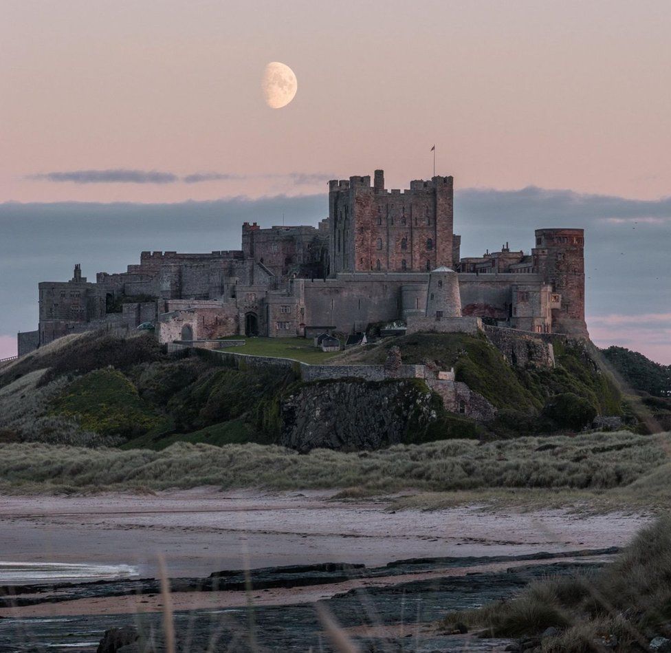 The moon in a pink sky above a grand castle on a cliff top