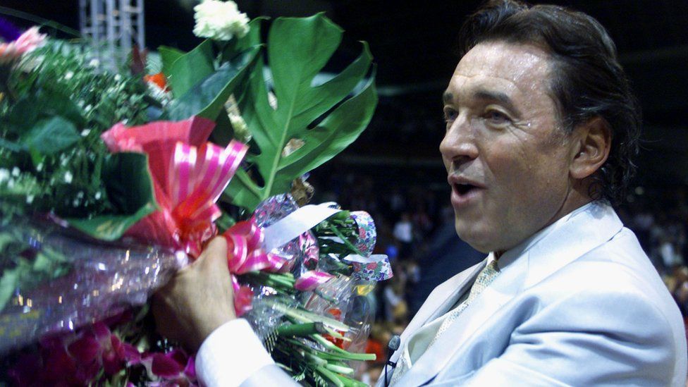 Karel Gott carries flowers from the stage during a Gala Show on his 60th birthday in Prague Sports Hall in 1999