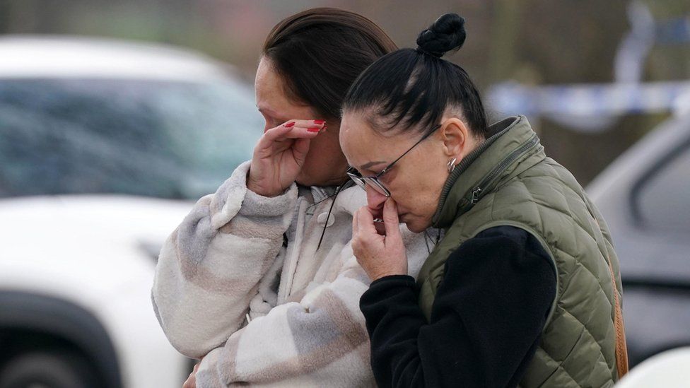 Upset mourners look at the flowers and tributes near to Babbs Mill Park in Kingshurst