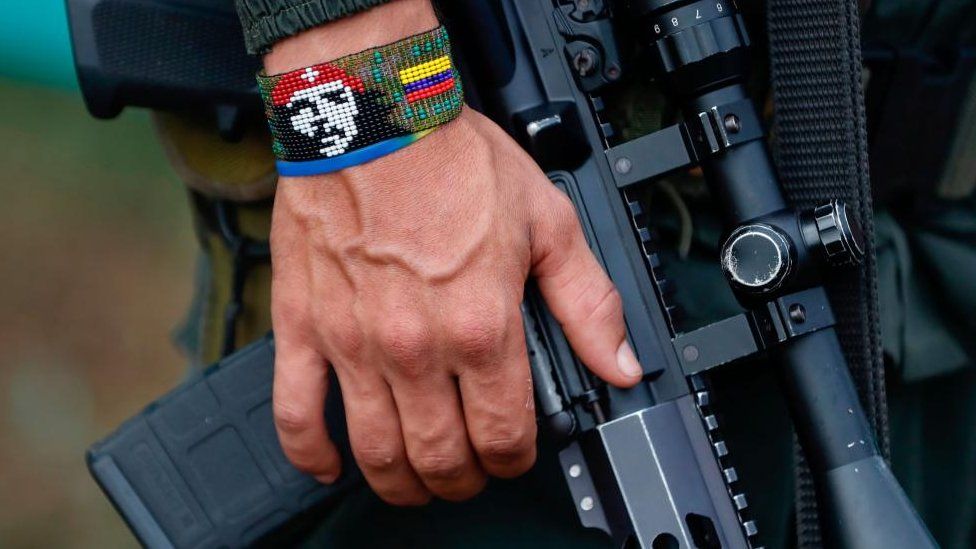 A man wearing a bracelet with the colours of the Colombian flag and a picture of Che Guevara holds a rifle at a gathering of Farc dissidents, in Casa Roja, Colombia, 16 April 2023