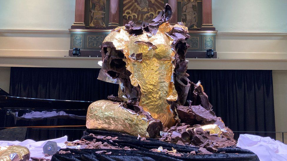A smashed sculpture with the head gone, covered in bits of gold foil