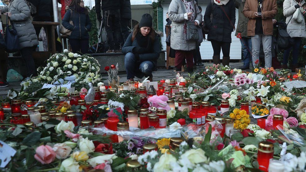 Mourners lay flowers and candles at a makeshift memorial near the site where a man drove a heavy truck into a Christmas market in an apparent terrorist attack