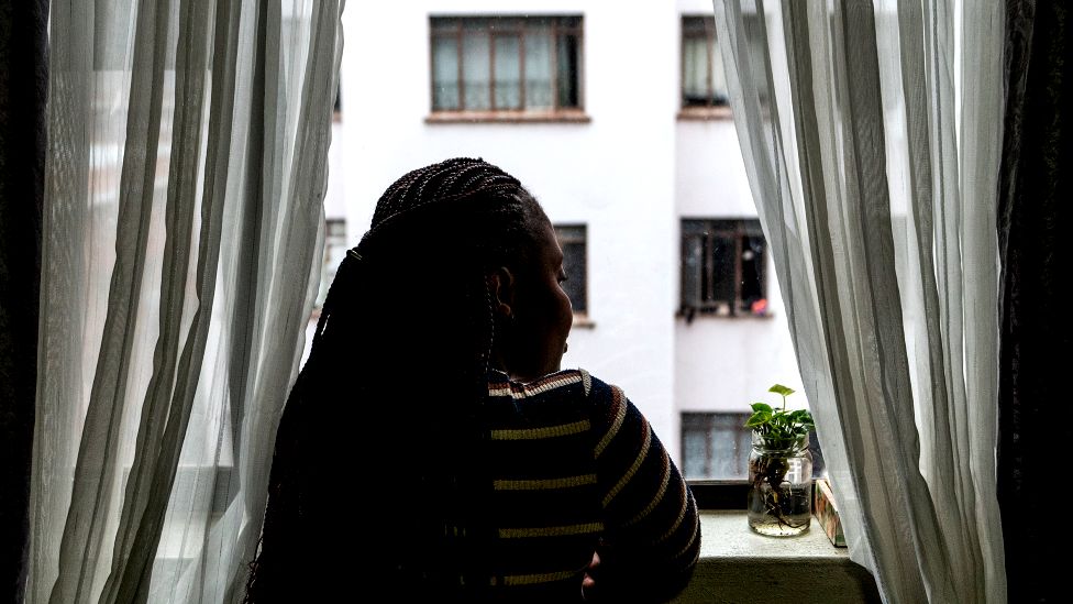 Зимбабвийская женщина смотрит из окна в Хиллброу, Йоханнесбург, Южная Африка