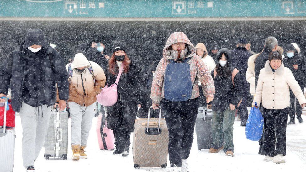Travelers walk in the snow at the exit of a railway station in Huaibei in central China's Anhui province