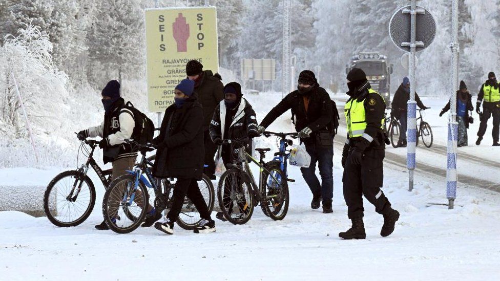 Finnish border guards and migrants with bicycles walk near the border crossing between Finland and Russia, at Salla, Lapland, Finland November 21, 2023