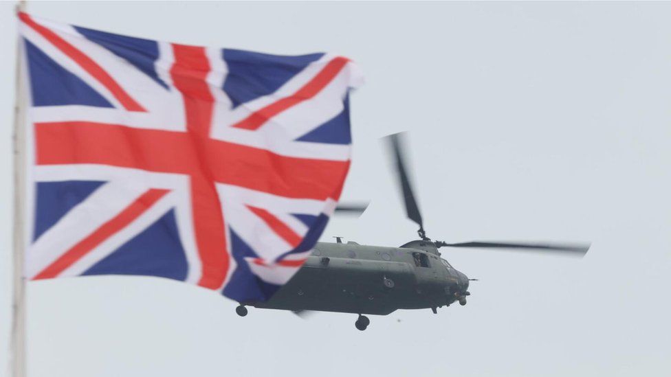 helicopter in sky next to British flag