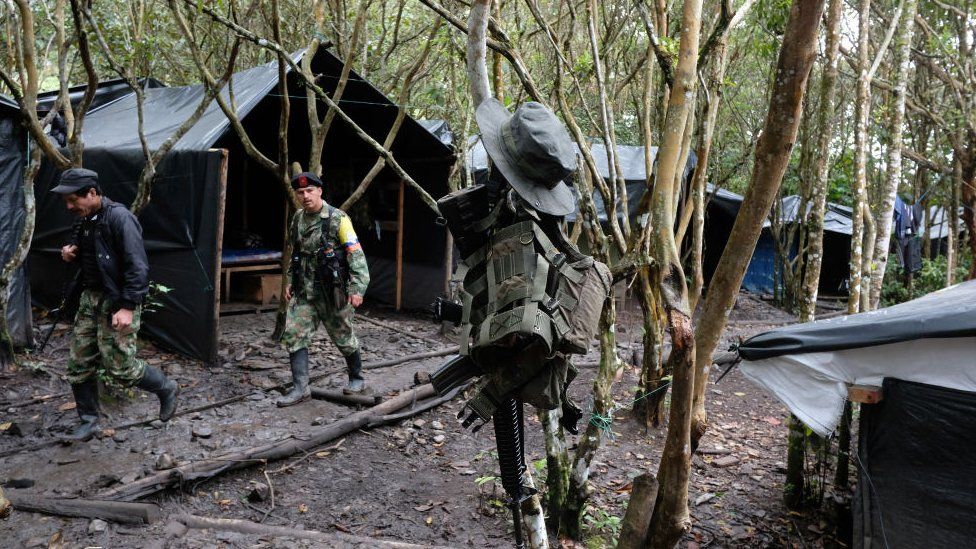 A general view inside a demobilization camp where two FARC fighters pass by an automatic assault rifle and a vest hanging on a tree on January 17, 2017 in Vereda La Elvira, Colombia.