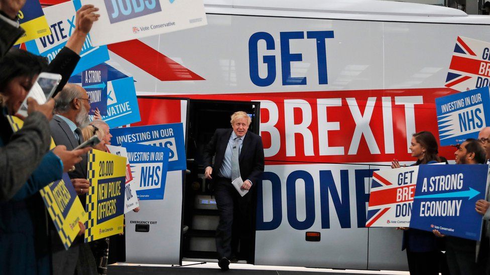 Boris Johnson comes out of a bus which bears the slogan "get Brexit done" in Union Jack colours