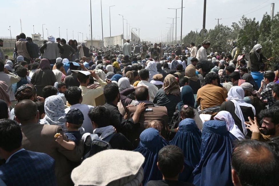 Афганцы собираются на обочине дороги возле военной части аэропорта в Кабуле 20 августа 2021 года, надеясь бежать из страны после военного переворота талибов